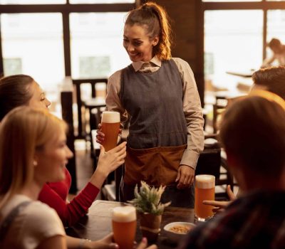 Happy waitress serving beer to group of friends in a bar. Happy waitress serving beer to group of young people in a pub.